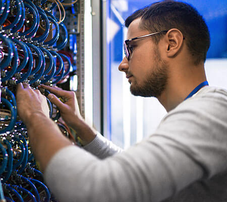 Man with computer touching multi colored wires in various wall panels