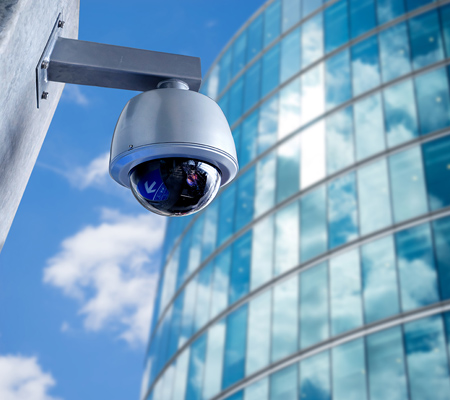 Video Surveillance Camera outside with blue sky and glass building to the right