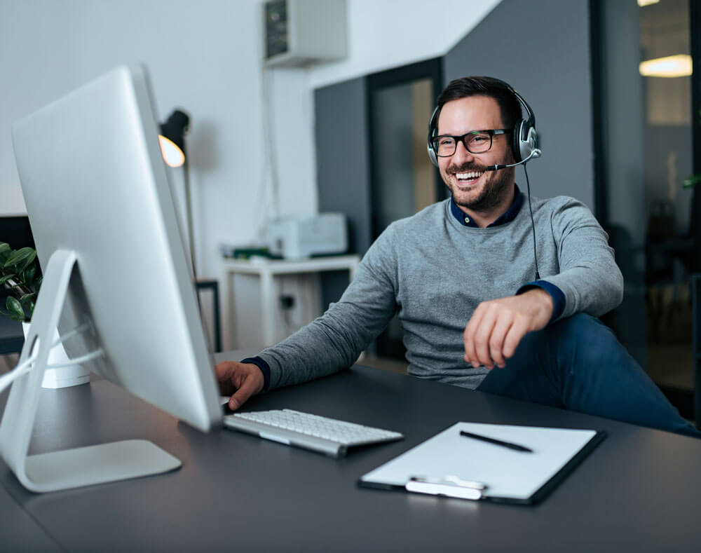 A man sitting at a computer smiling while using his VoIP phone system.